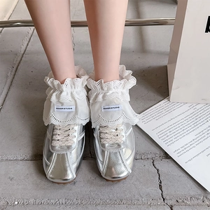 Close-up of silver metallic sneakers with wide white lace trim and bow knot detail