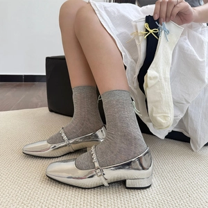 Detail of grey mesh socks with a silk bow on the heel paired with silver Mary Jane shoes