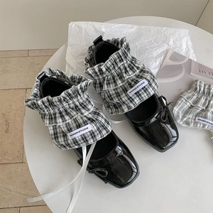 Close-up of black patent leather Mary Jane shoes with plaid ruffle trim and bow detail