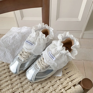 Detail of silver metallic sneakers with large white lace trim and beige braided laces