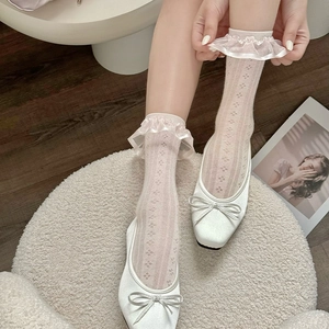 Close-up of pink lace hollow mesh socks styled with white bow flats and a magazine