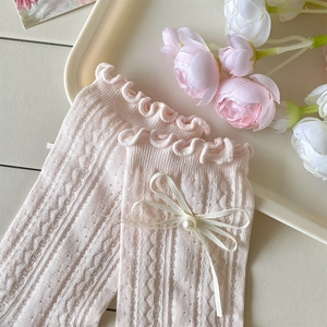 Détail de chaussettes en résille rose clair avec motifs cœur, bord festonné et nœud
