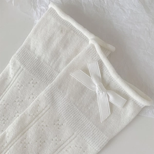 Detail of white mesh knit ballet style socks with satin bow and delicate hollow pattern