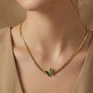 Close-up of a model wearing a green enamel butterfly pendant on a gold Cuban chain