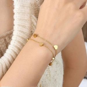Detailed view of layered gold heart bracelet on wrist with cozy white knit background