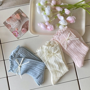 Détail de chaussettes à volants avec nœuds et perles en bleu, beige et rose