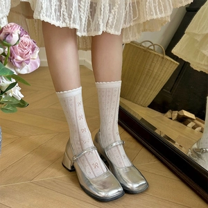 Detail of white hollow mesh crew socks with pink bow embroidery and silver Mary Jane shoes