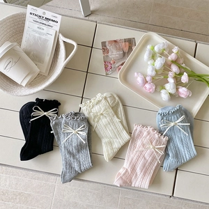 Détail de poignets à volants avec nœuds en soie et perles sur chaussettes en maille torsadée