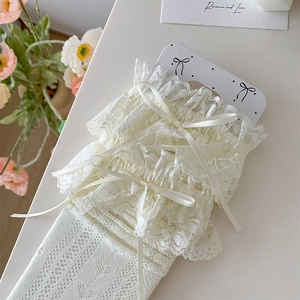 Dettaglio di calze al ginocchio color crema con pizzo, fiocco e maglia traforata