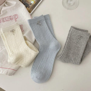 Detail of cable knit crew socks with silver metal bow charms in cream, blue, and grey