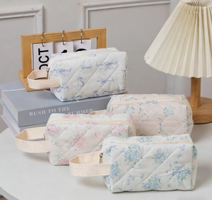 Quilted floral cosmetic bags with cat prints and metal zippers on a white desktop