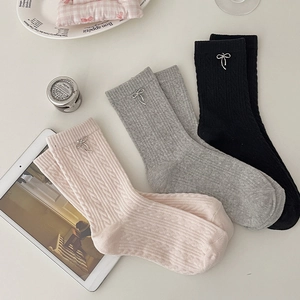 Detail of cable knit crew socks in pink, grey and black with metal bow charm accents