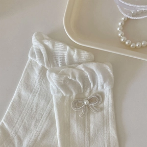 Detail von weißen Rüschensocken mit bestickter Schleife und Perle auf einem Tablett