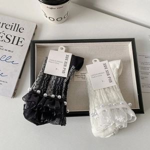 Détail de chaussettes en résille avec froufrous en dentelle et perles en noir et blanc