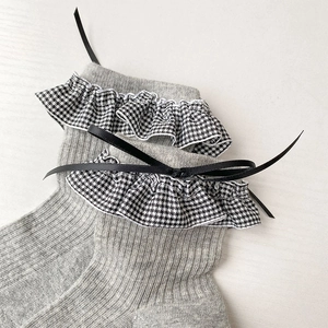 Détail de chaussettes grises avec bords à volants pied-de-poule et nœuds noirs décoratifs
