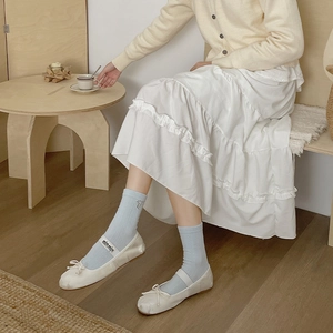 Detail of light blue cable knit socks with metal bow charm and white ballet shoes