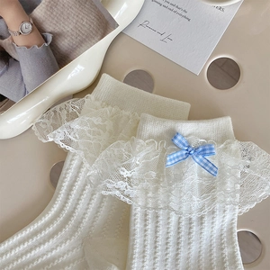 Détail de chaussettes Lolita blanches avec dentelle délicate et un nœud à carreaux bleu