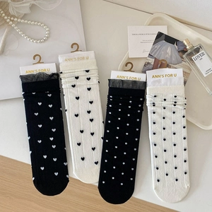 Détail de chaussettes en dentelle avec motifs de cœurs et pois en noir et blanc à plat