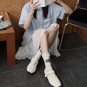 Close-up of white Mary Jane sneakers with ruffled lace socks and chic woven labels