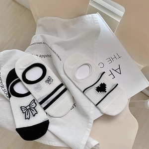 Détails de trois chaussettes basses avec motifs nœuds et cœurs sur lin blanc