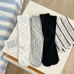 Flat lay of knit mid-calf socks with hollow diamond pattern in white, grey, and black