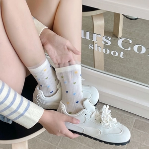Détail de chaussettes en résille blanche à cœurs colorés et bordure en dentelle fine