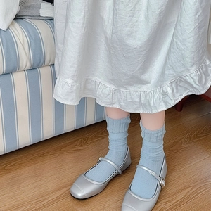 Détail de chaussettes en maille bleu clair avec babies argentées sur un sol en bois