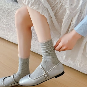 Detail of grey polka dot crew socks styled with silver Mary Jane shoes and lace skirt