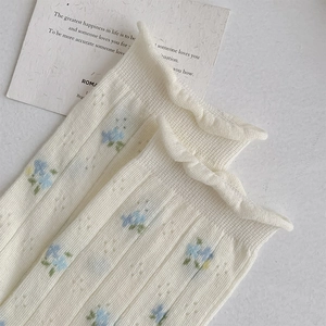 Detailed close-up of cream socks with blue floral pattern and ruffled lettuce edges