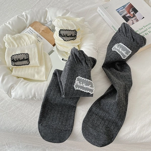 Detail of ribbed knit crew socks with lace trim and fabric label in cream and charcoal