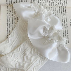 Close-up of white cable knit socks featuring elegant satin ruffle trim on an open book