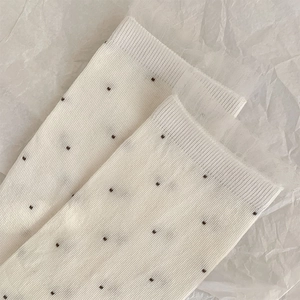 Close-up of cream lace mesh socks featuring small dark polka dots and layered frill detail