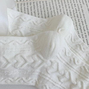 Macro detail of white knit socks with heart patterns and silk ribbon bow accent
