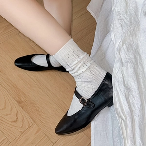 Close-up of black matte Mary Jane shoes with white ribbed socks on wooden floor