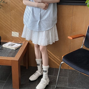 Close-up of white Mary Jane sneakers with ruffled socks and blue plaid skirt outfit