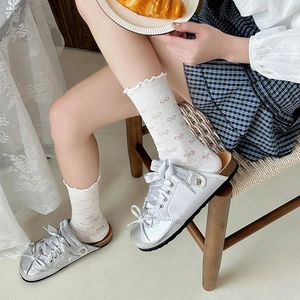 Close-up of white ruffle socks with bow patterns paired with silver bow mule shoes