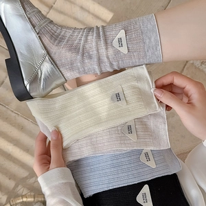 Detailed view of grey ribbed mid-calf socks with a triangular logo and silver loafers