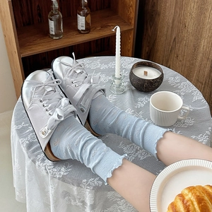 Light blue ruffle socks with bow patterns paired with satin shoes in a cozy home setting