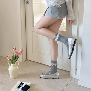 Detail of grey lace trim socks with bow accents paired with silver Mary Jane shoes
