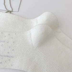 Close-up of white ribbed knit socks featuring sparkling rhinestones and vertical texture