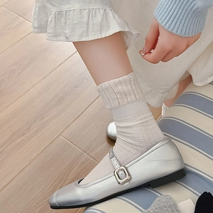 Gros plan de chaussettes en maille ajourée beige portées avec des ballerines argentées