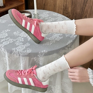 Detail of white ruffle socks with bow patterns paired with pink suede athletic sneakers
