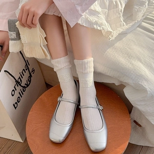 Detail of white cotton socks with Lucky label and silver Mary Jane shoes on a stool