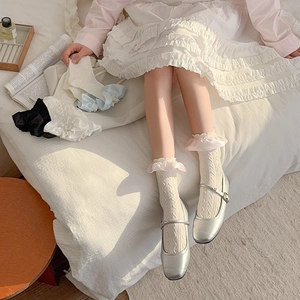 Detailed view of lace ruffle trim socks paired with silver Mary Jane shoes on white bedding
