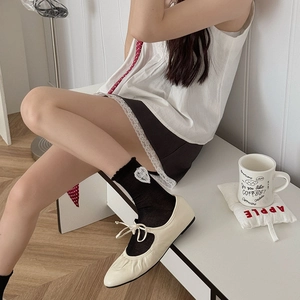 Détail de chaussettes en dentelle à cœurs noirs portées avec des ballerines
