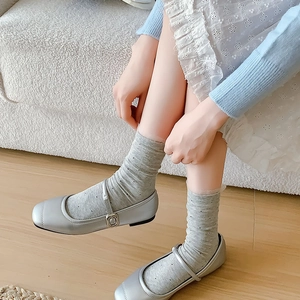Close-up of silver Mary Jane shoes paired with grey polka dot lace socks on wood floor