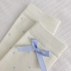 Detail of cream-white knit socks featuring blue polka dots and a satin bow decoration