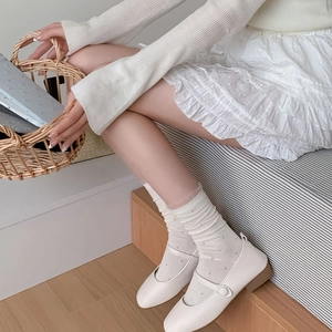 Close-up of cream Mary Jane flats paired with delicate polka dot tulle socks and a skirt