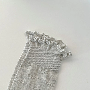 Detail of white ruffled lace cuff and delicate hollow bow pattern on the cotton sock