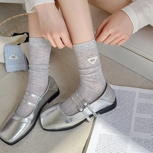Close-up of gray knit crew socks with triangle label worn with silver Mary Jane shoes
